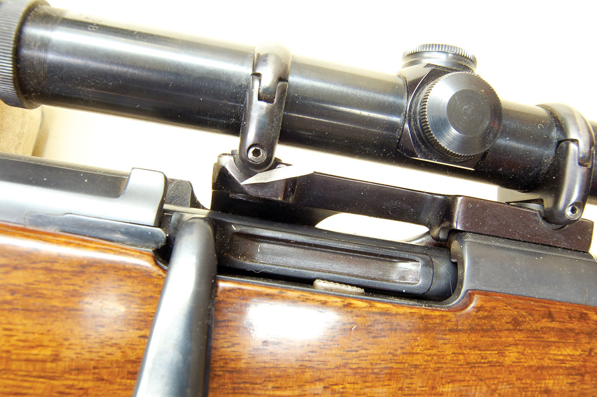 A scope based on a rebarreled Ml910 has the rear ring located ahead of the bridge with the base ground away (arrow) to allow the bolt handle to access the split bridge. It is a special Leupold Adjusto-Mount from the 1950s.